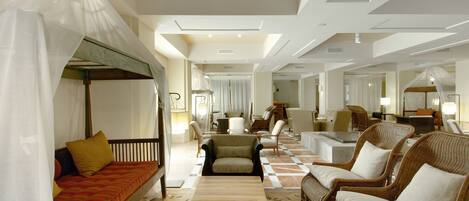 Un hall d’hôtel spacieux avec un sol à carreaux, plusieurs coins salon comprenant un canapé et des fauteuils, et un lit à baldaquin.