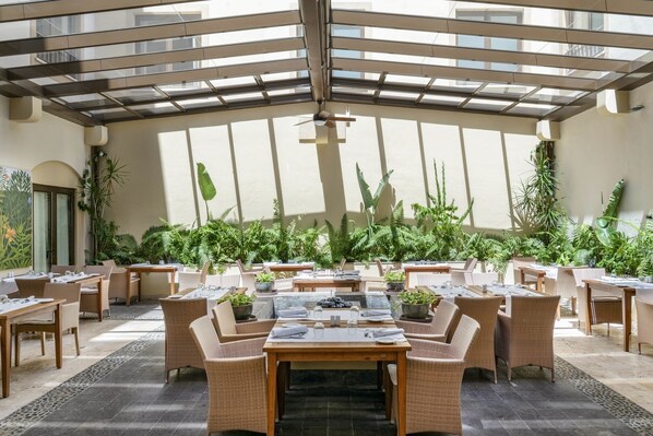 Un espacio de comedor al aire libre con techo, mobiliario de mimbre y plantas en macetas.