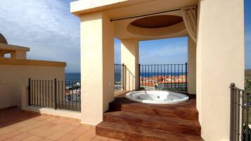 A rooftop terrace with a hot tub, a view of the sea, and a cityscape in the background.