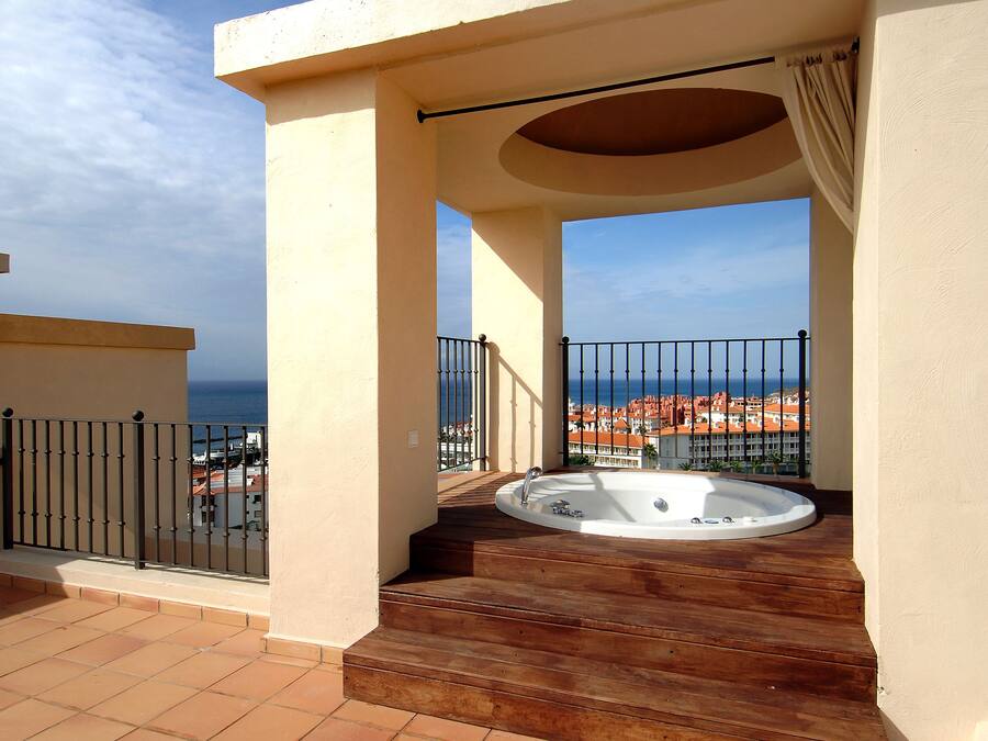 A rooftop terrace with a hot tub, a view of the sea, and a cityscape in the background.