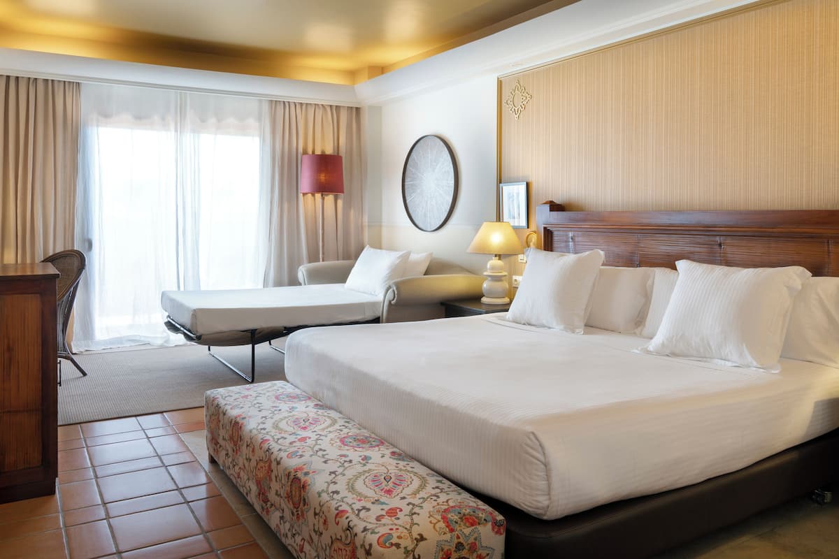 Une chambre d’hôtel avec un grand lit, un lit plus petit, un bureau et une chaise.