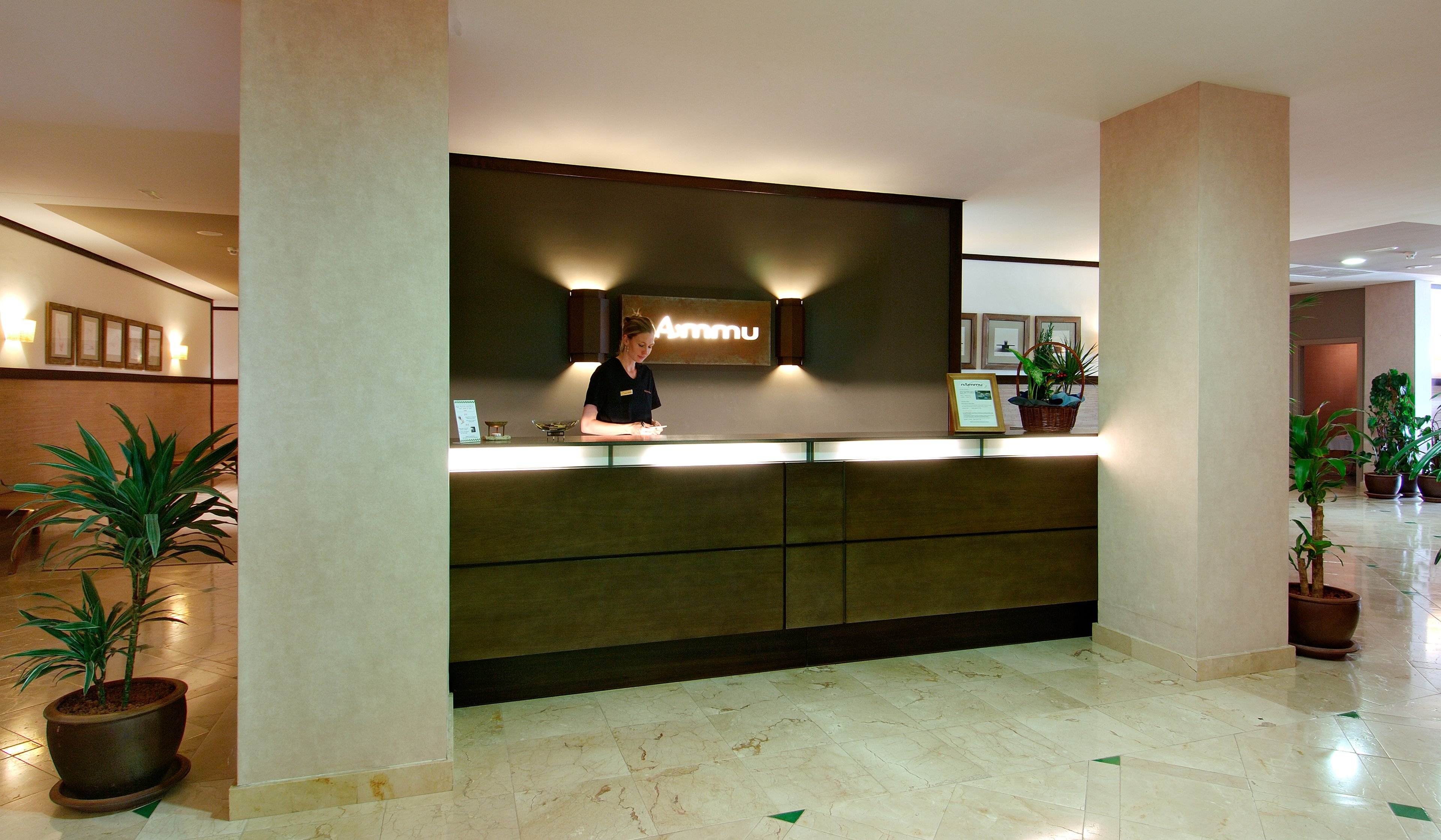 A reception desk with a sign above it, a potted plant to the left, and another to the right.