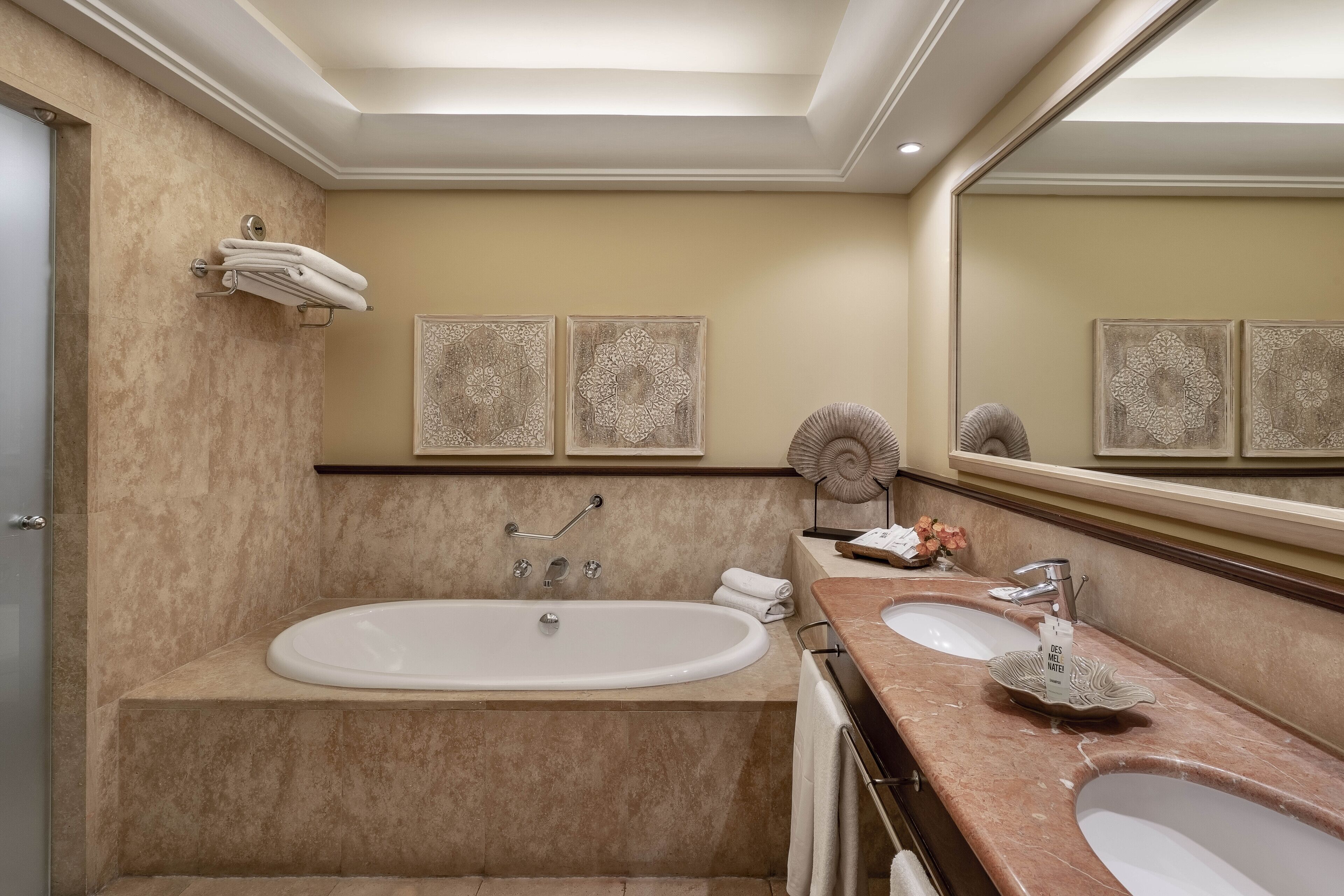 Un baño moderno con una bañera grande, dos lavamanos y decoración en la pared.