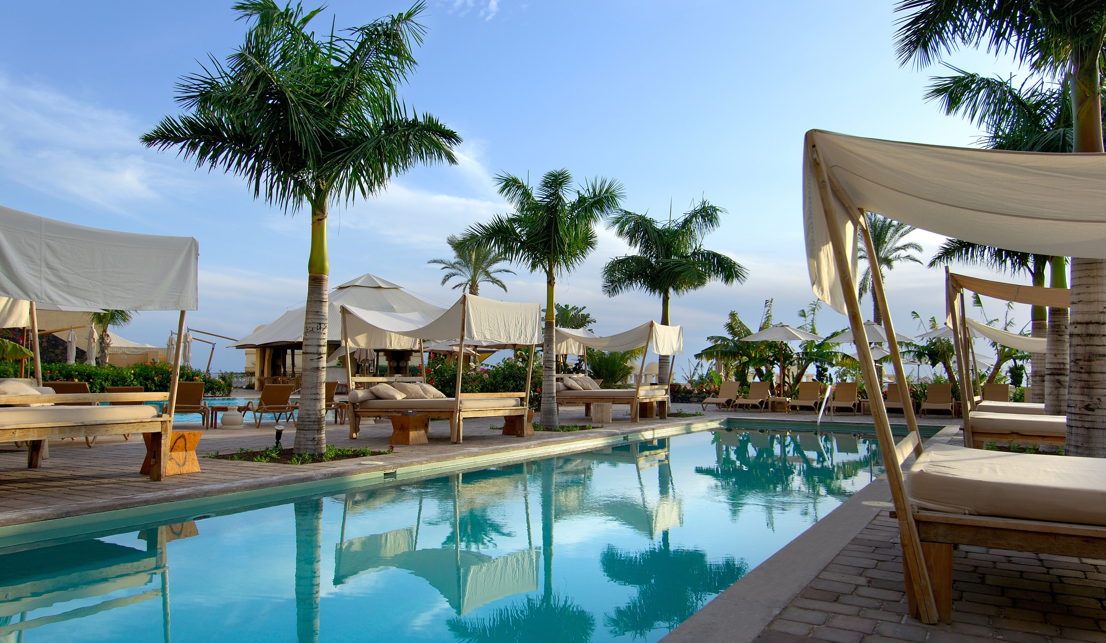 A poolside area with lounge chairs, umbrellas, and palm trees.
