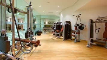 A gym with various exercise machines, a mirror, and a wooden floor.