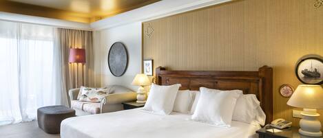 A hotel room with a large bed, a bedside table with a lamp, a chair, and a window with curtains.