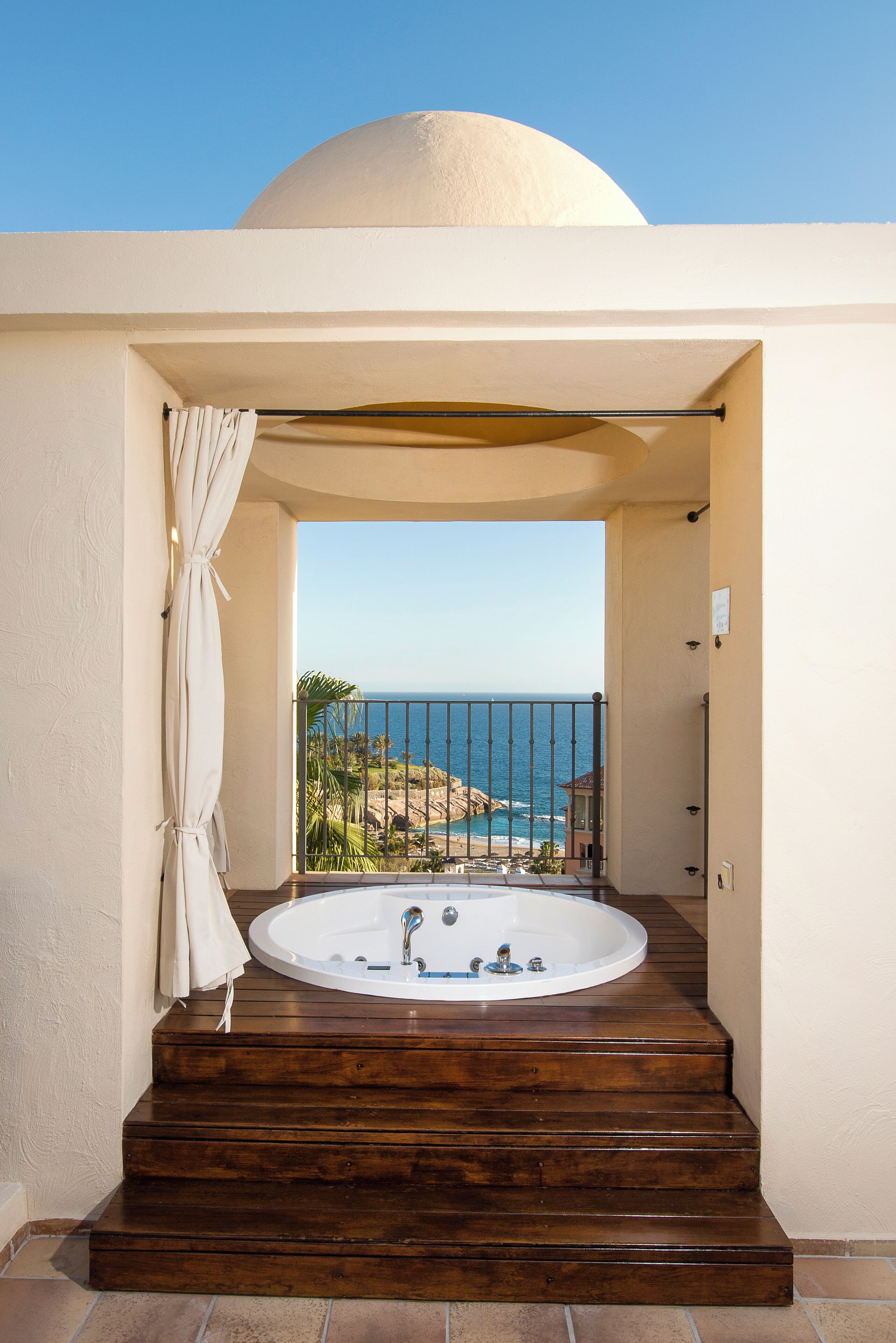 Uma banheira de hidromassagem com degraus que levam a uma varanda com vista para o oceano.