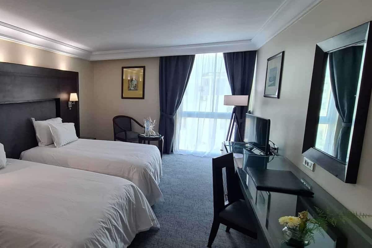 A hotel room with two beds, a desk with a TV, a chair, and a desk lamp.