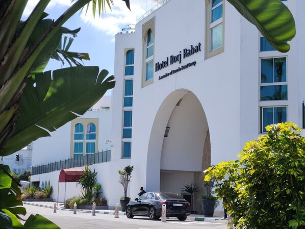 A modern hotel building with a prominent arched entrance and a clear sign reading "Hotel Borj Ribat."