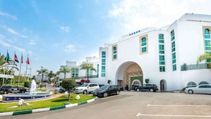 A modern building with a large arched entrance, multiple flags, and a parking lot with several cars. - Hotel Borj Rabat – A member of Barcelo Hotel Group (Rabat)