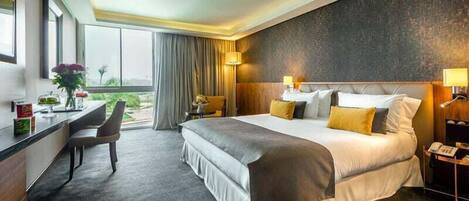 Une chambre d’hôtel avec un grand lit, un bureau avec une chaise, une table de chevet avec une lampe et une vue sur l’extérieur par la fenêtre.