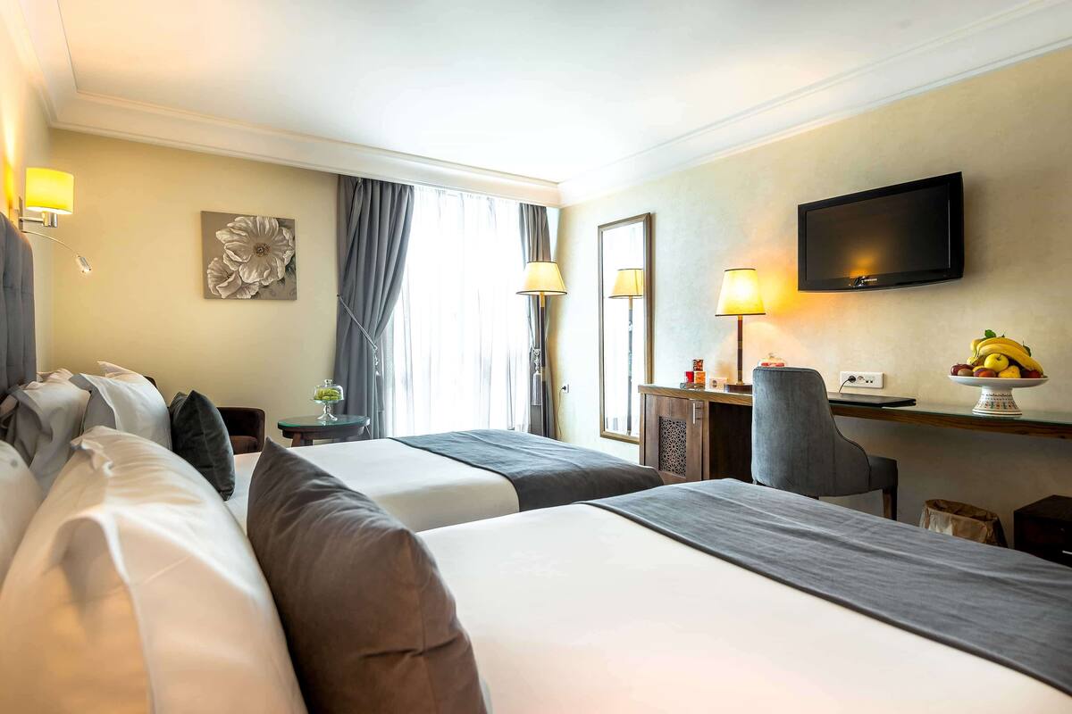 A hotel room with two beds, a desk, a chair, a television, and a fruit bowl.