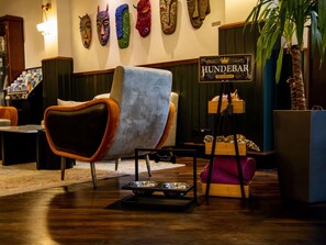 A lounge area with a plush armchair, a wooden dog bed, a sign for Hundebar VIP service, and a wall with colorful masks.