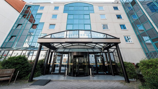 The Mercure Hotel entrance with a glass facade, a covered entrance, and a red-roofed building to the left. - Mercure Hotel Frankfurt Airport Langen (Langen)