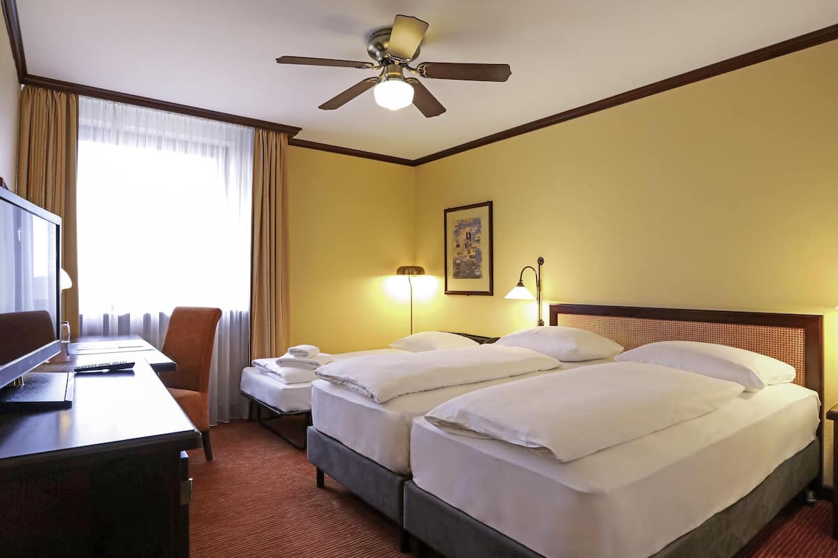 Une chambre d’hôtel avec deux lits, un bureau avec une télévision, un ventilateur de plafond et une fenêtre avec des rideaux.