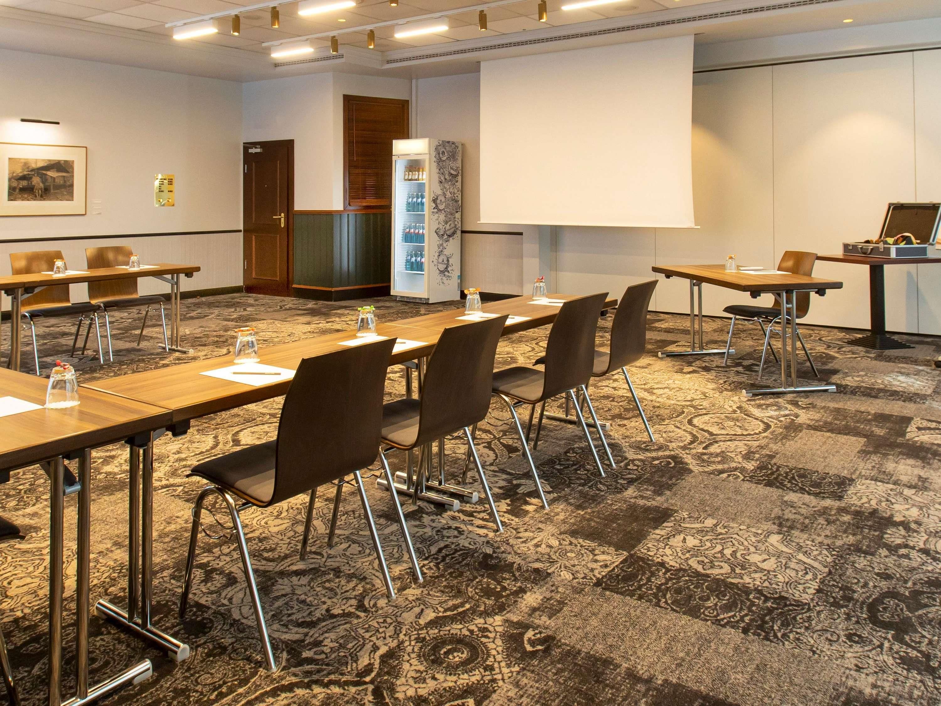 A conference room with a large table, chairs, a projector screen, and a refrigerator.