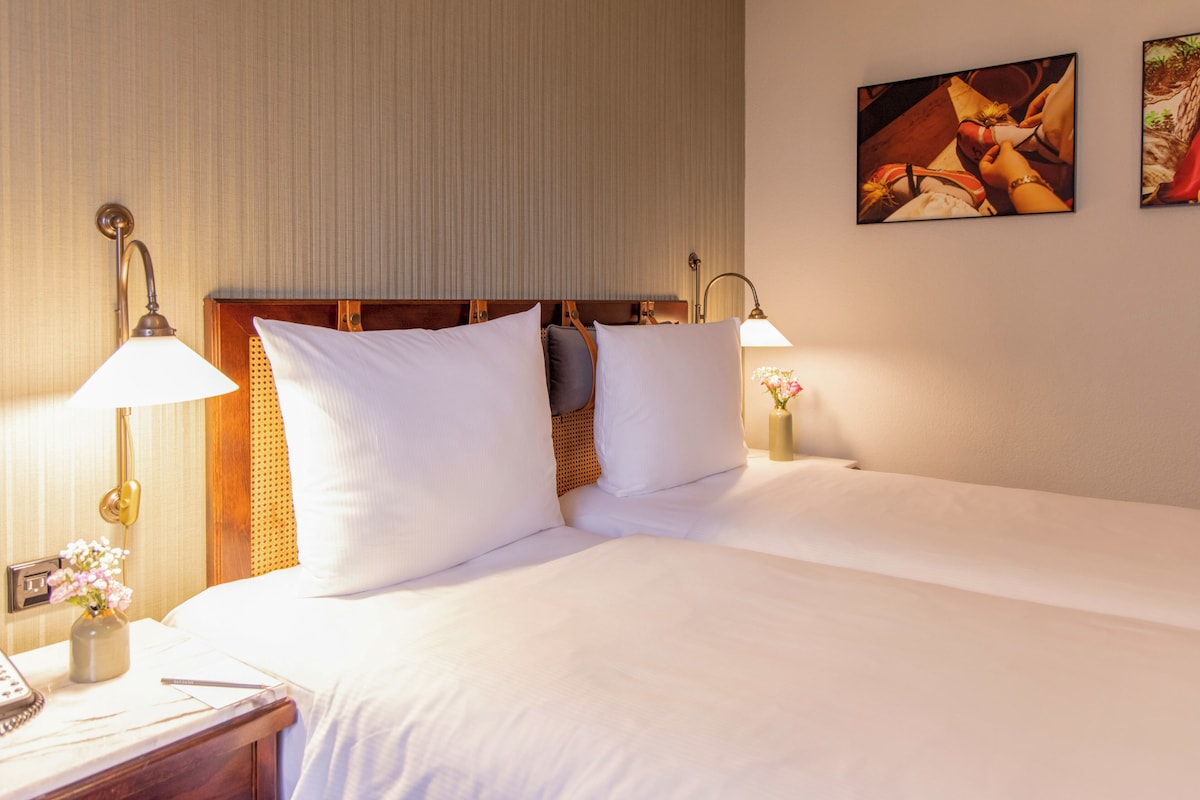 A neatly made bed with white linens and two bedside lamps.