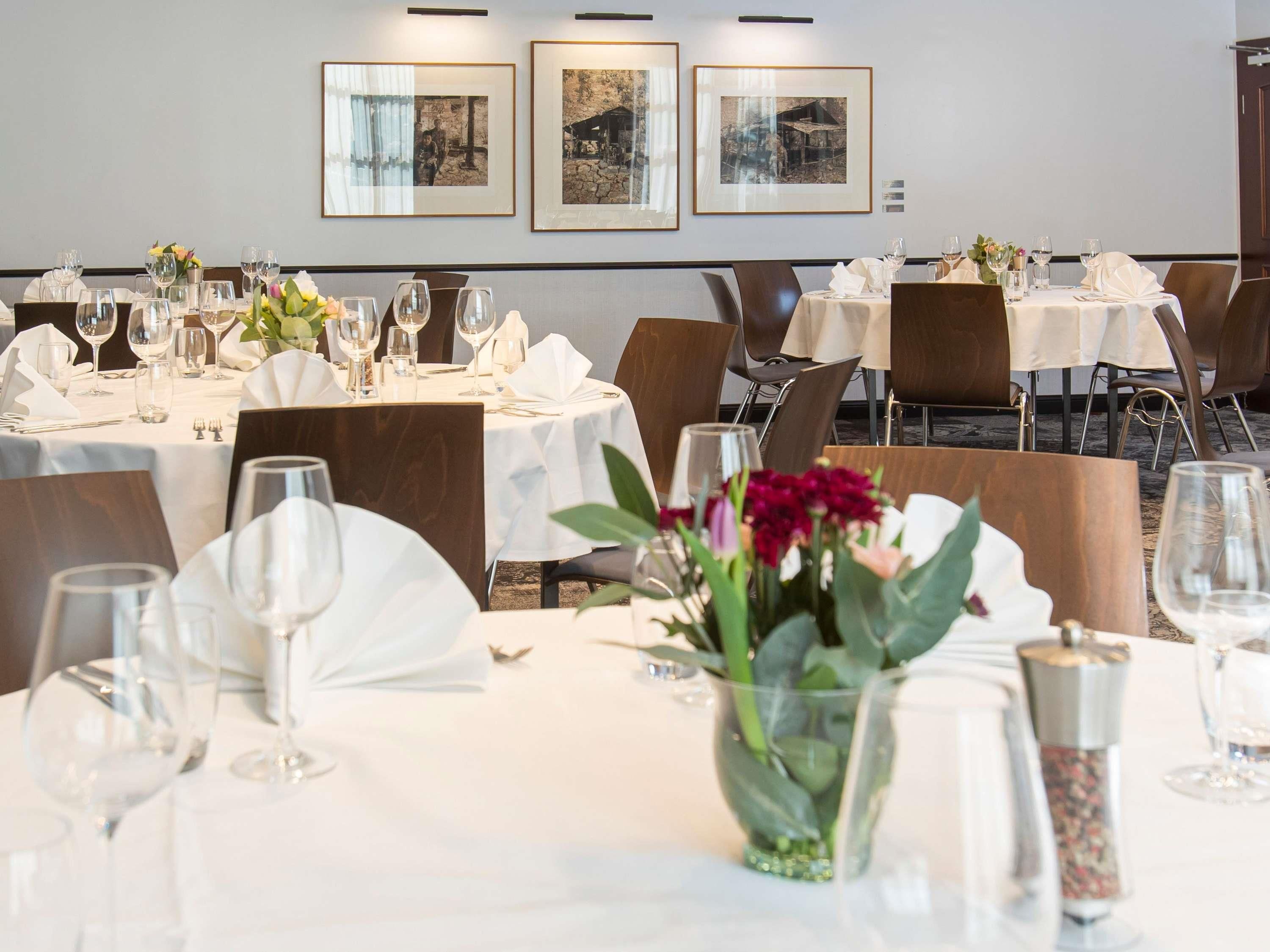 Un comedor con mesas preparadas para el servicio, cuadros en la pared y un jarrón con flores sobre la mesa.