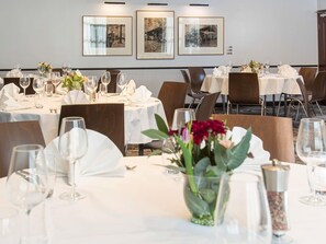 Un comedor con mesas preparadas para el servicio, cuadros en la pared y un jarrón con flores sobre la mesa.