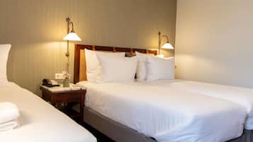 A hotel room with two single beds, a bedside table with a lamp, a phone, and a vase with flowers.