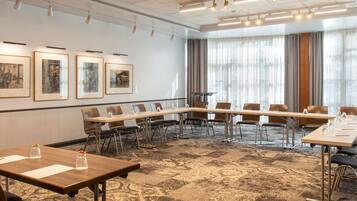 A conference room with a long table, chairs, framed pictures on the wall, and large windows with curtains.