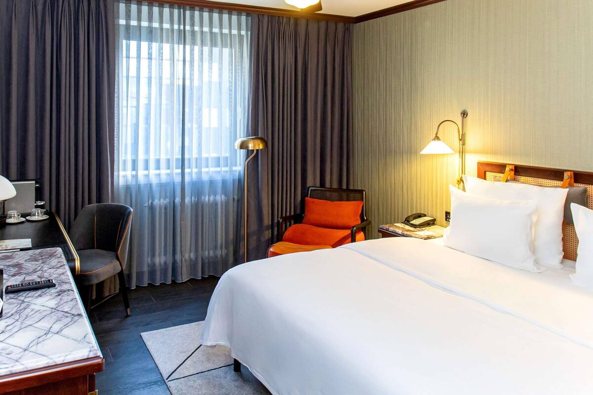 Une chambre d’hôtel équipée d’un lit, d’un bureau, d’une chaise, d’un ventilateur de plafond et d’une fenêtre avec des rideaux.