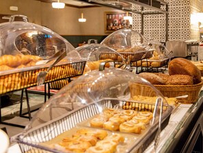 A buffet with various baked goods like bread and pastries under protective covers.