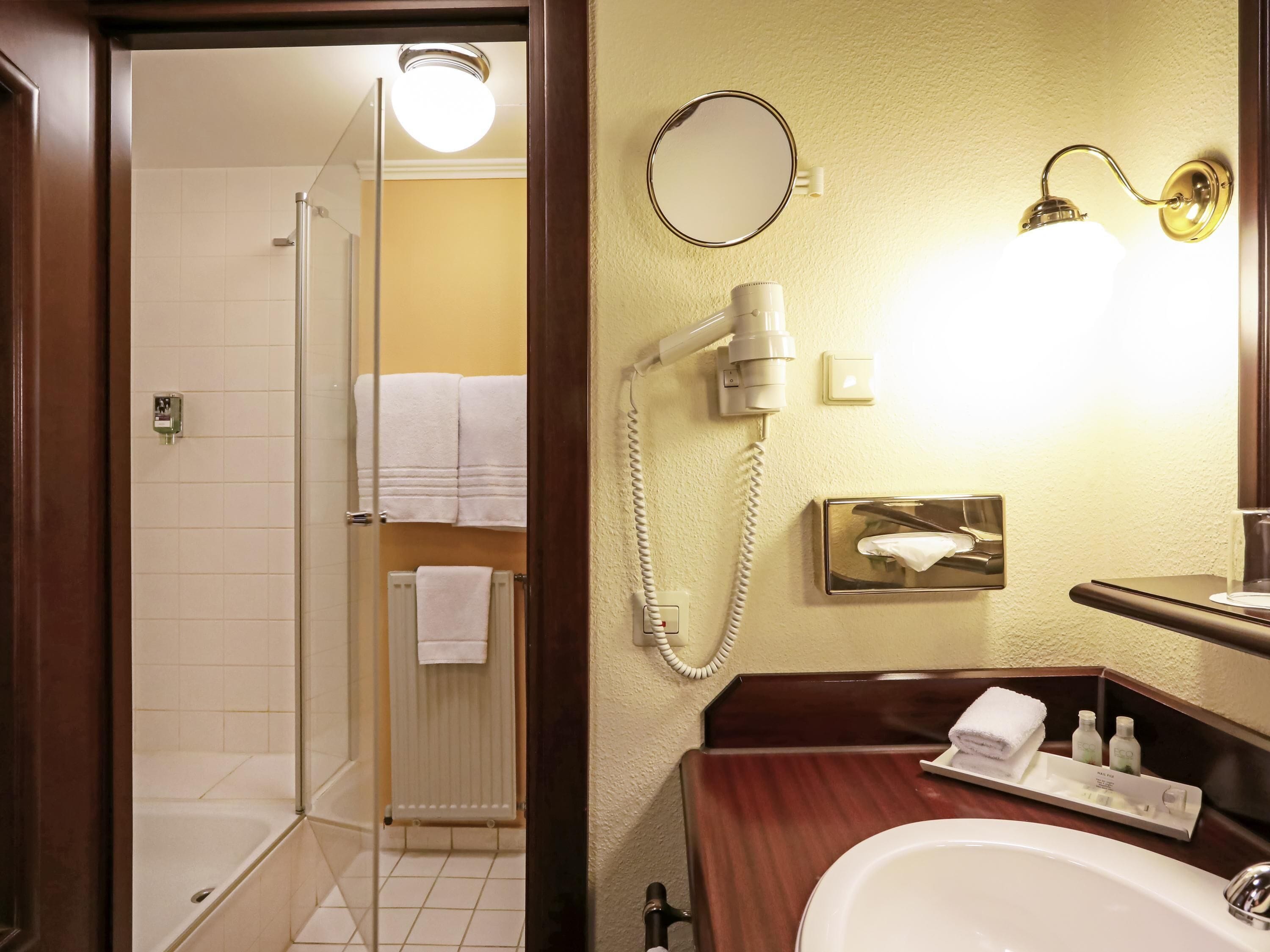 Un bagno con doccia, lavabo, specchio e asciugacapelli.