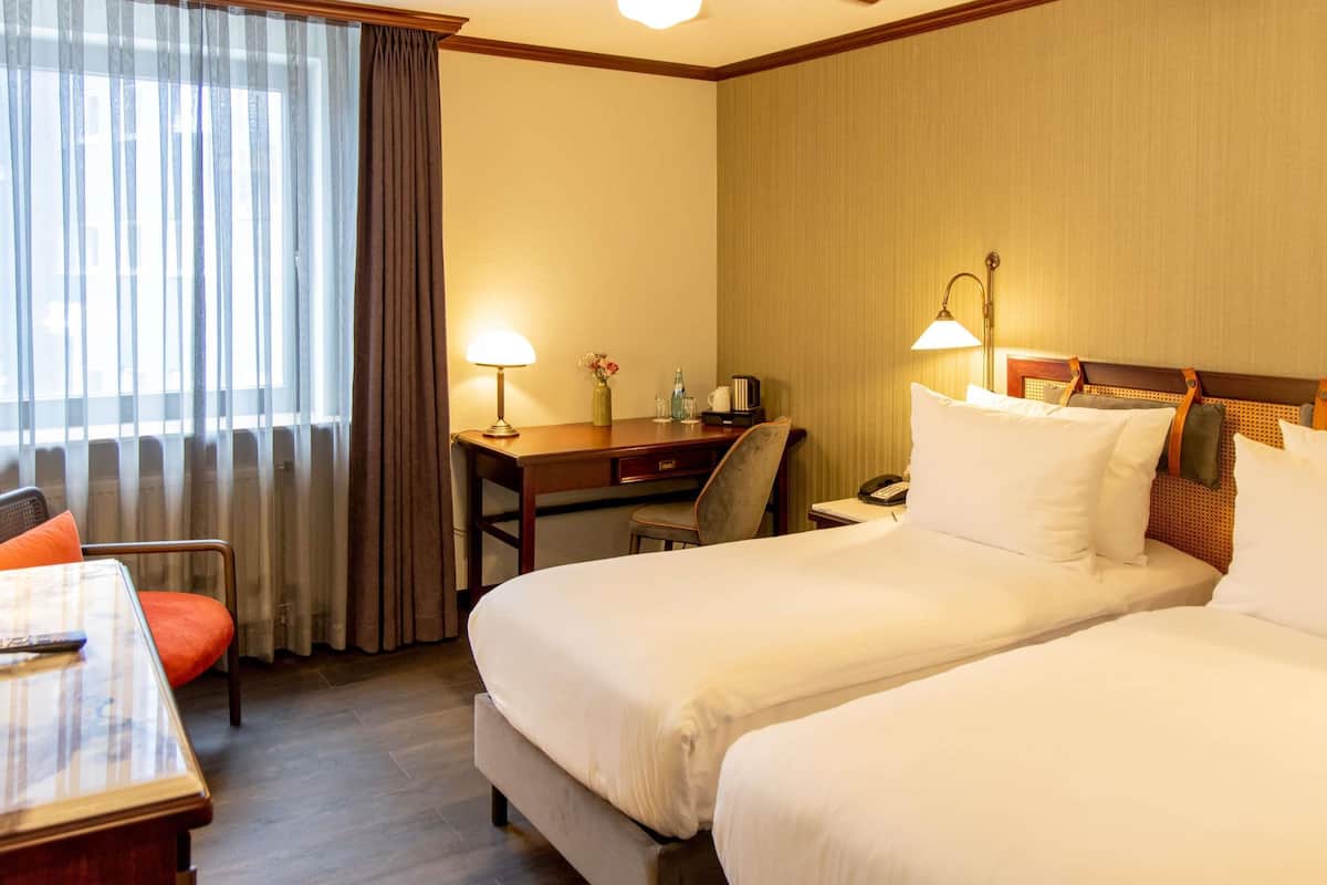 Une chambre d’hôtel avec deux lits, un bureau, une chaise, un téléphone et un ventilateur de plafond.