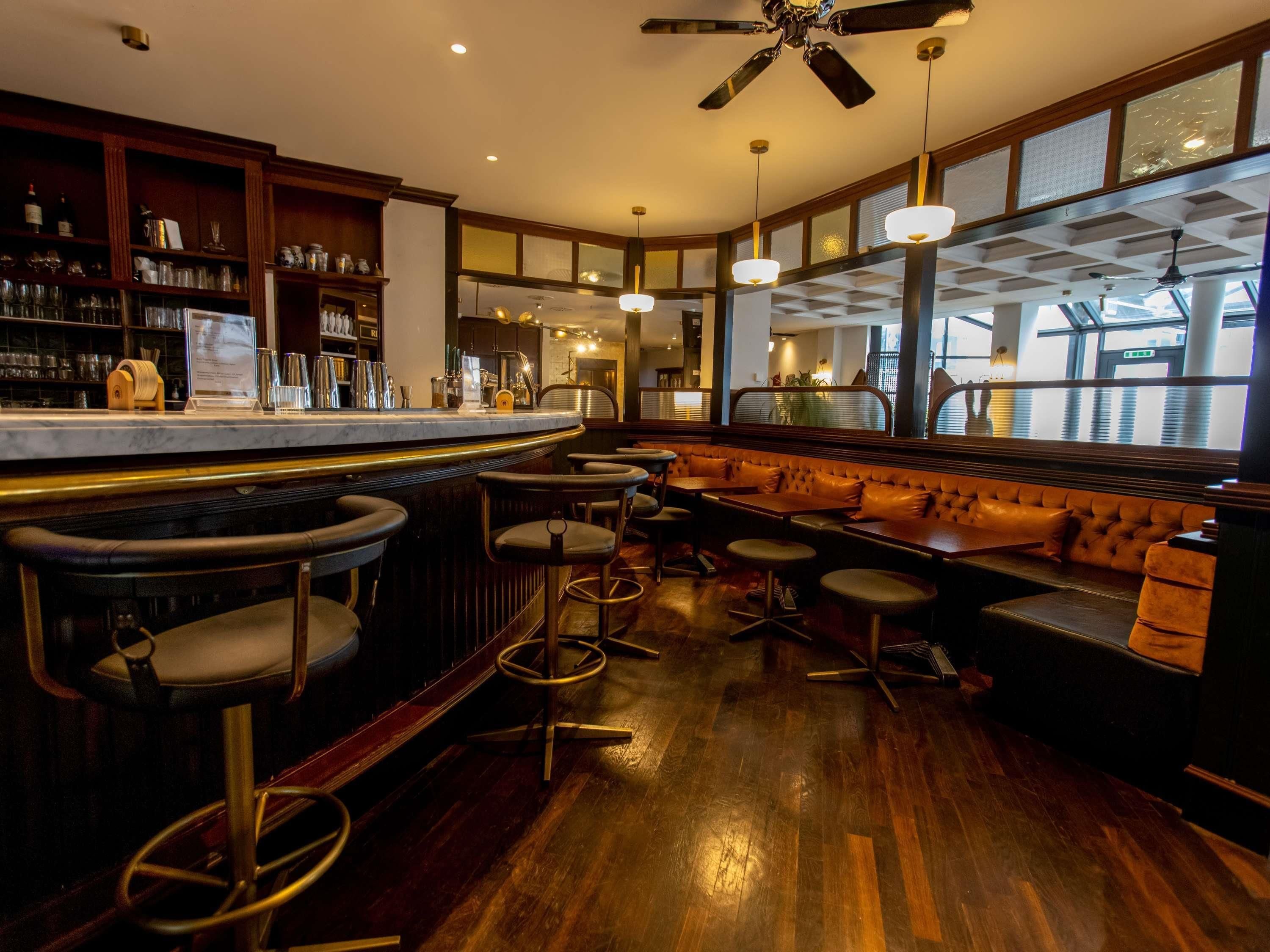 A bar area with wooden bar stools, a seating area with cushioned benches, and a large window providing a view of the outside.