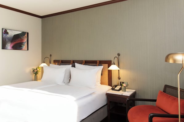 A hotel room with a neatly made bed, two bedside lamps, a telephone, and a chair.