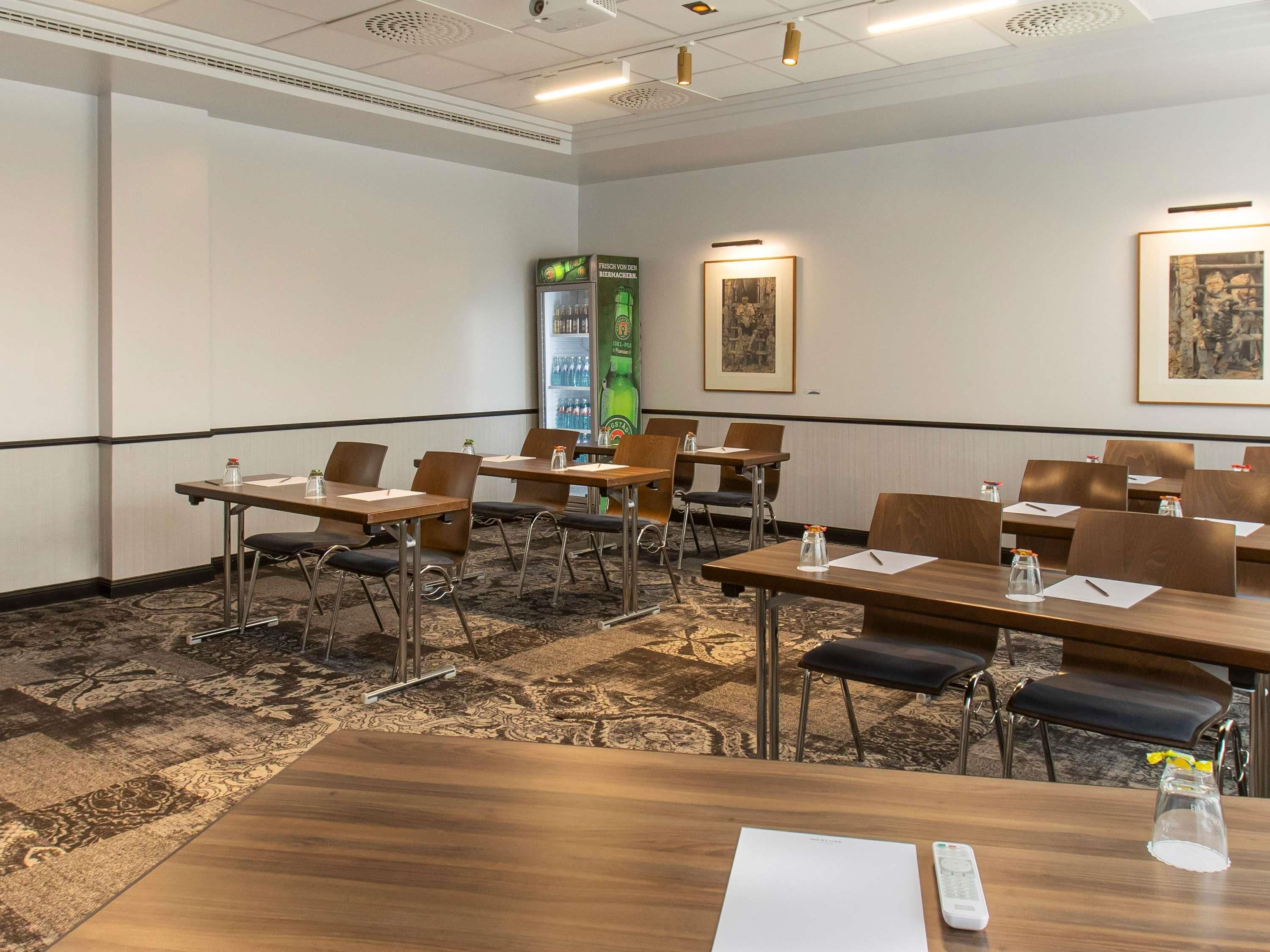 Een vergaderzaal met tafels, stoelen, een koelkast en kunstwerken in lijsten aan de muren.