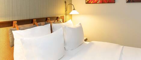 Ein Hotelzimmer mit einem Bett, Kissen, einem Kopfteil, einer Wandleuchte und zwei gerahmten Bildern.