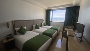 A hotel room with two beds, a desk, a chair, and a large window with a view of the sea. - Hotel Azur (Casablanca)