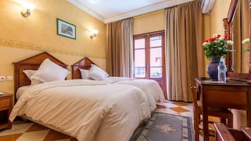 Habitación de hotel con dos camas, cabecera de madera, mesita de noche, escritorio con un florero y alfombra estampada.