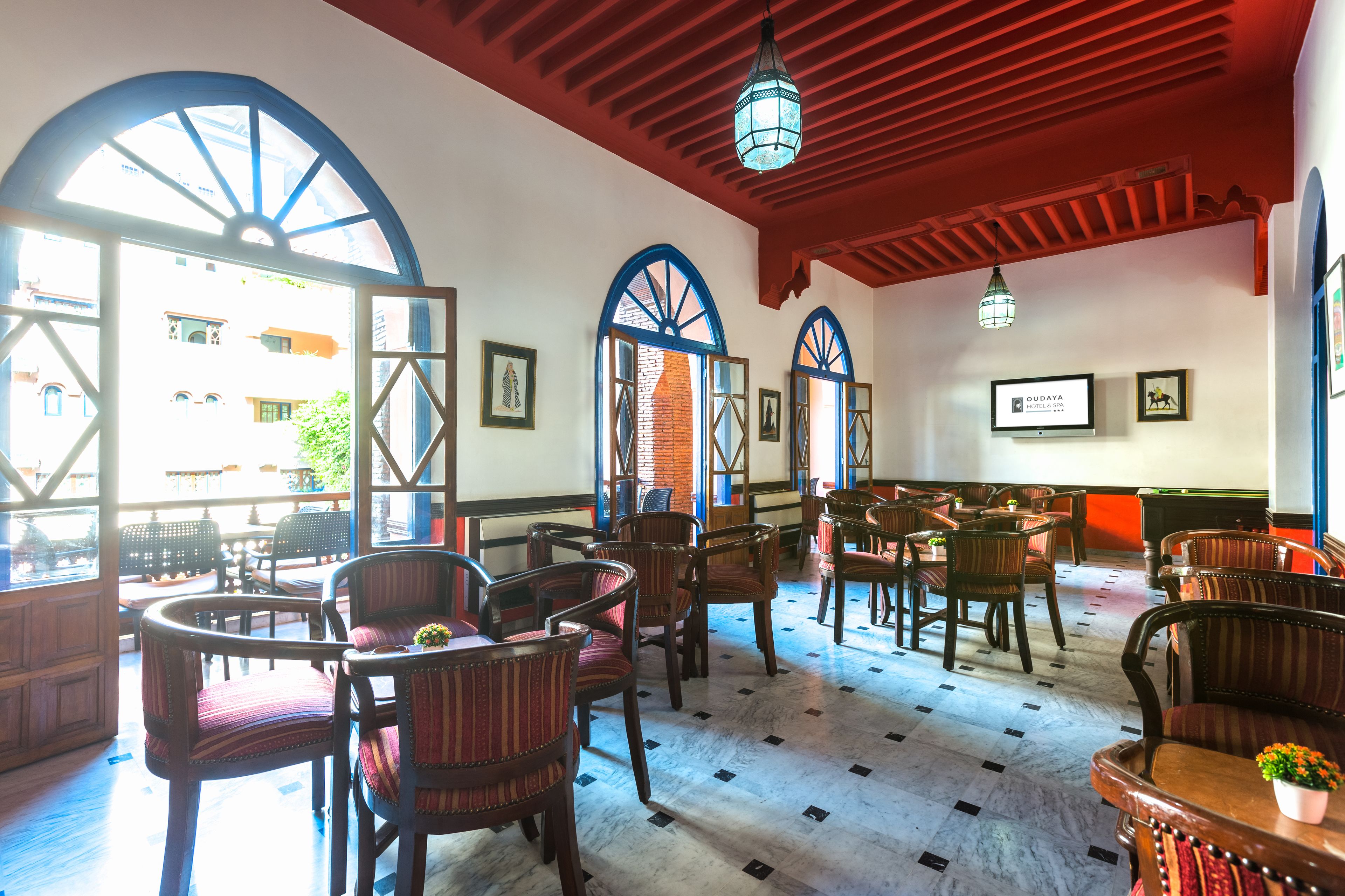 A hotel lobby with wooden furniture, large arched windows, and a red ceiling.