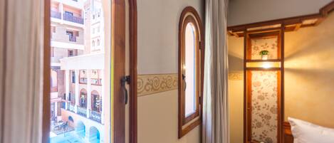 A hotel room with a view of a courtyard, a wooden wardrobe, and a bedside table with a lamp.