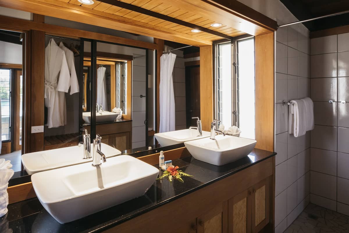 A modern bathroom with three sinks, wooden ceiling, and a large mirror.