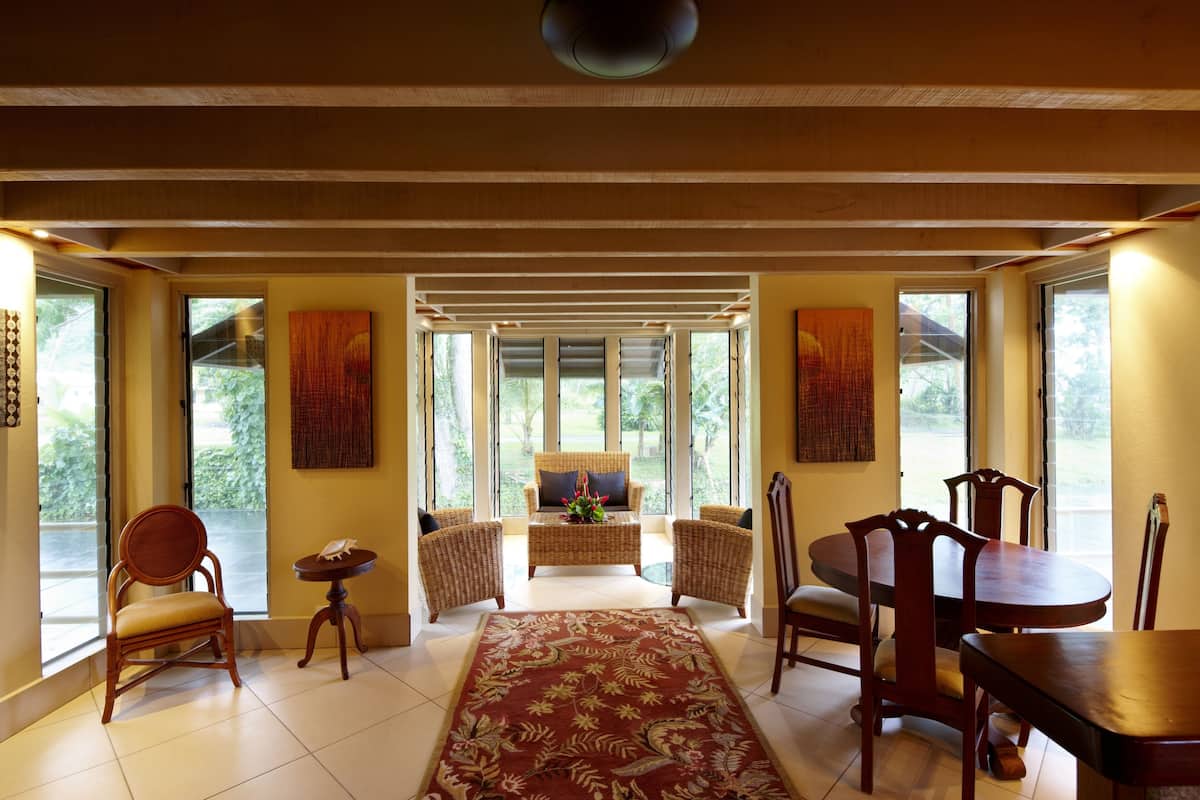 A spacious living area with a sofa, chairs, a dining table, and a large window providing a view of greenery.