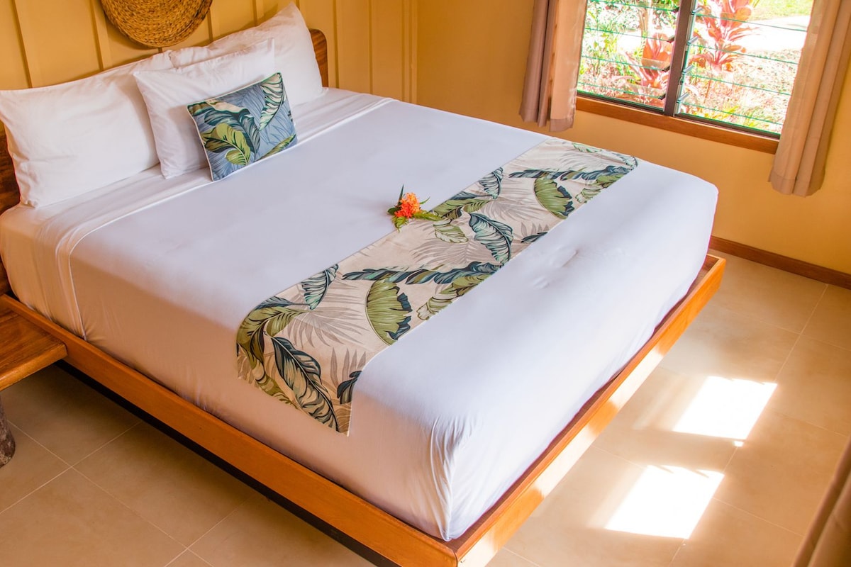 A bed with a leaf-patterned bedspread, a wooden headboard, and a window with curtains.