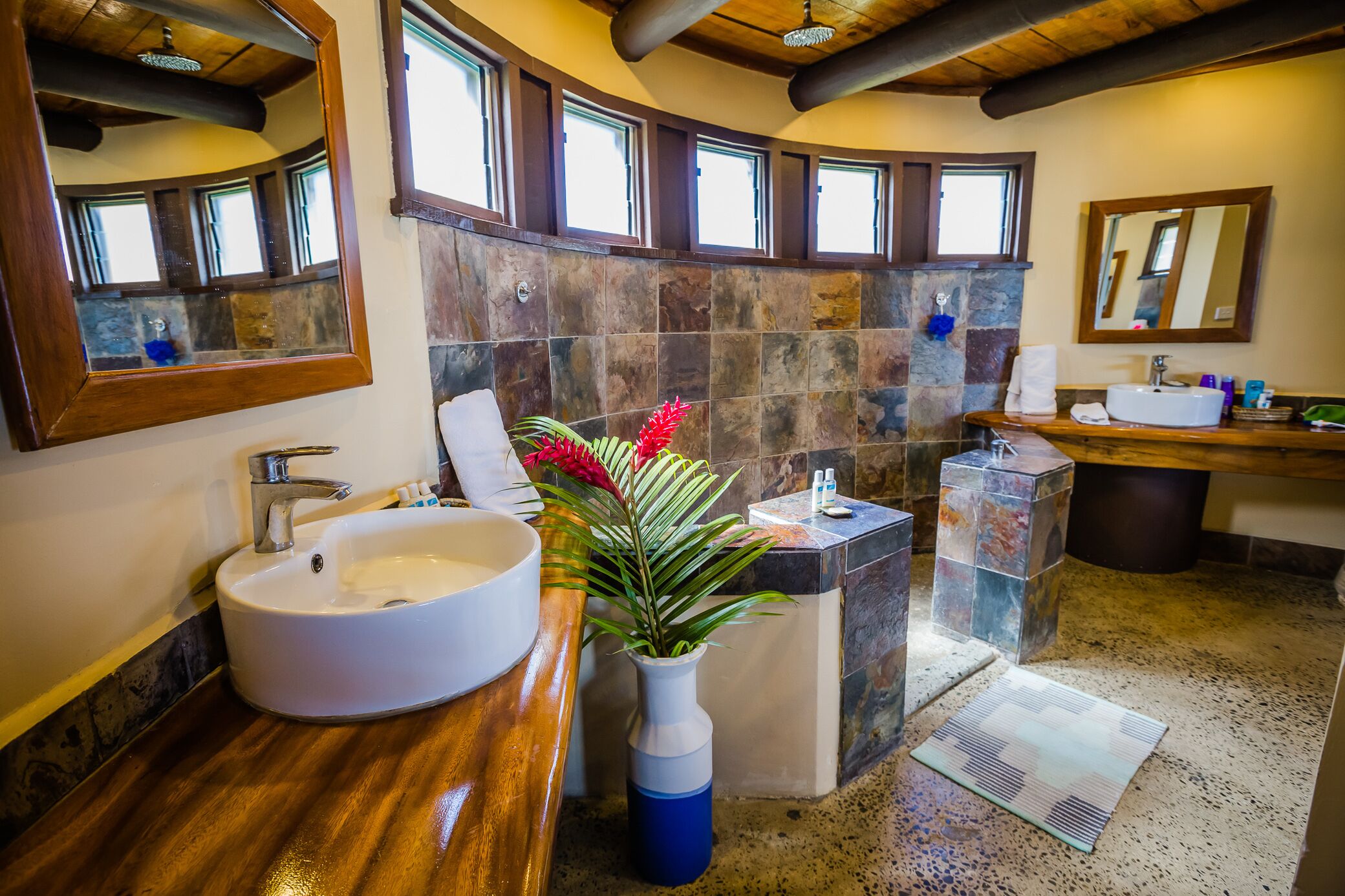 A bathroom with a large white sink, a wooden vanity, a mirror, and a stone wall.