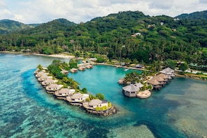 Et over vandet resort med bungalows forbundet af gangstier, omgivet af krystalklart turkis vand og frodig vegetation.