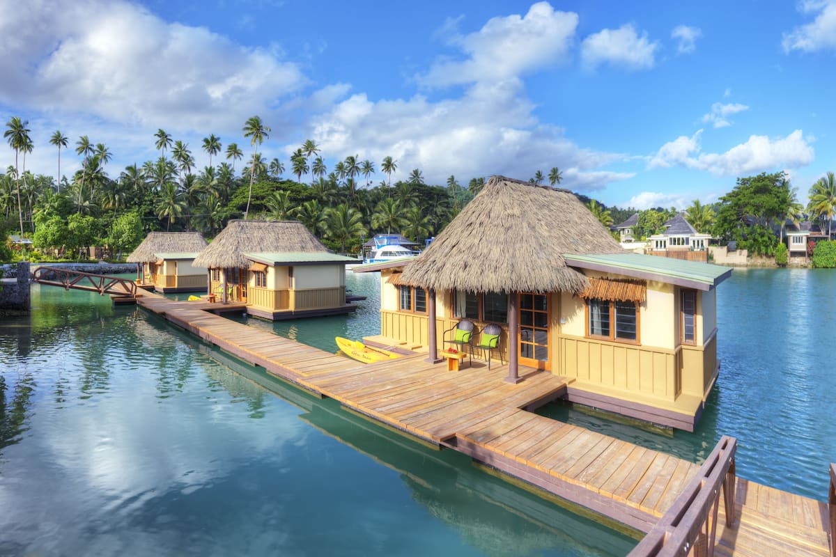 Overwater bungalows with thatched roofs, wooden walkways, and clear blue waters.