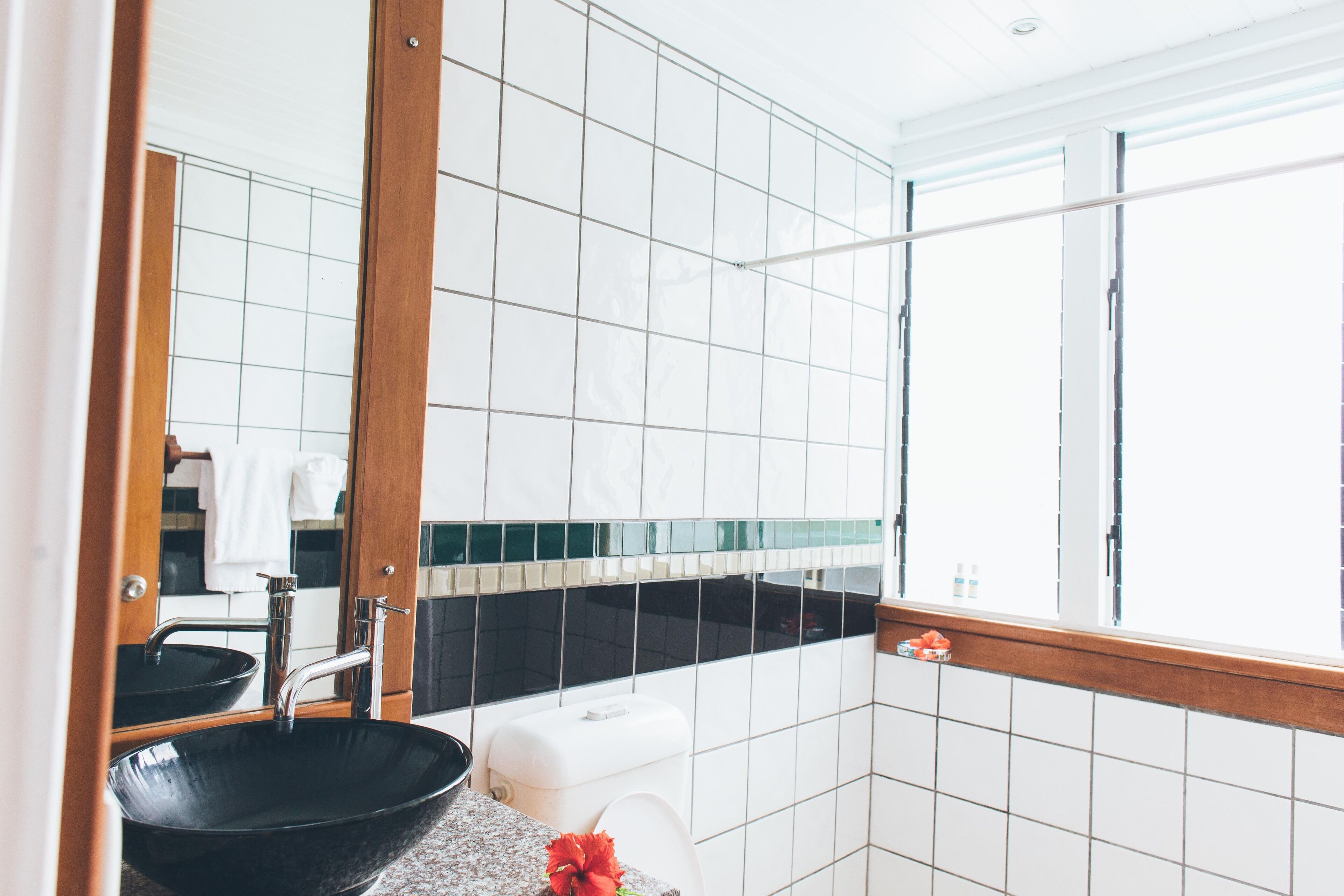 Ein Badezimmer mit einem schwarzen Waschbecken, weißen Fliesen, einem Fenster mit Holzrahmen und einem Spiegel.