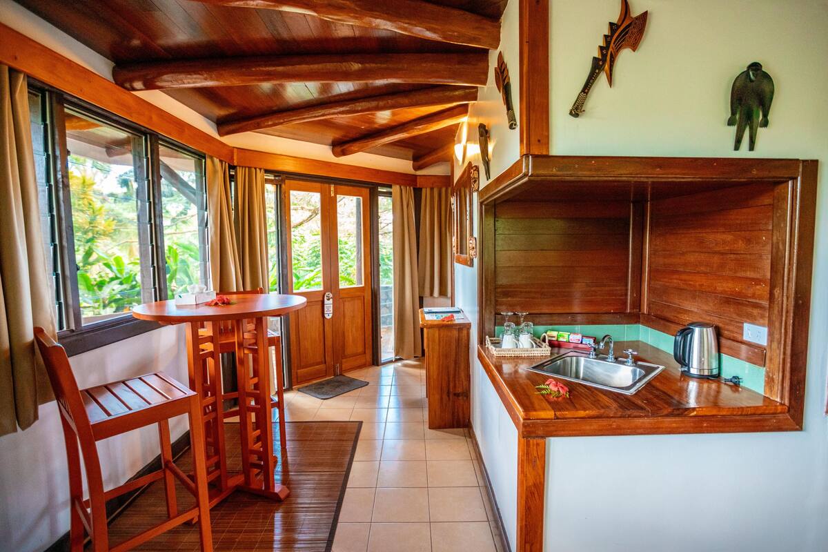 A wooden interior with a kitchen area, including a sink, a coffee maker, and a dining table with chairs.
