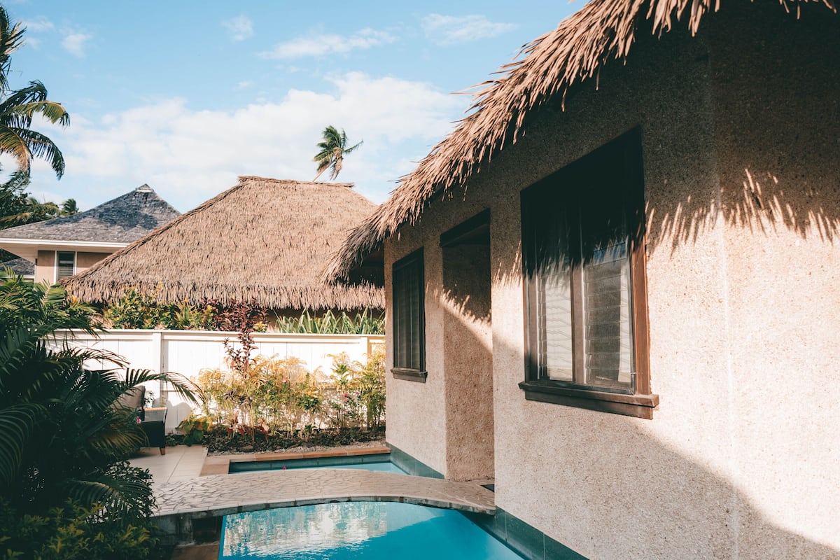 A pool area with a thatched-roof building, clear blue sky, and palm trees.