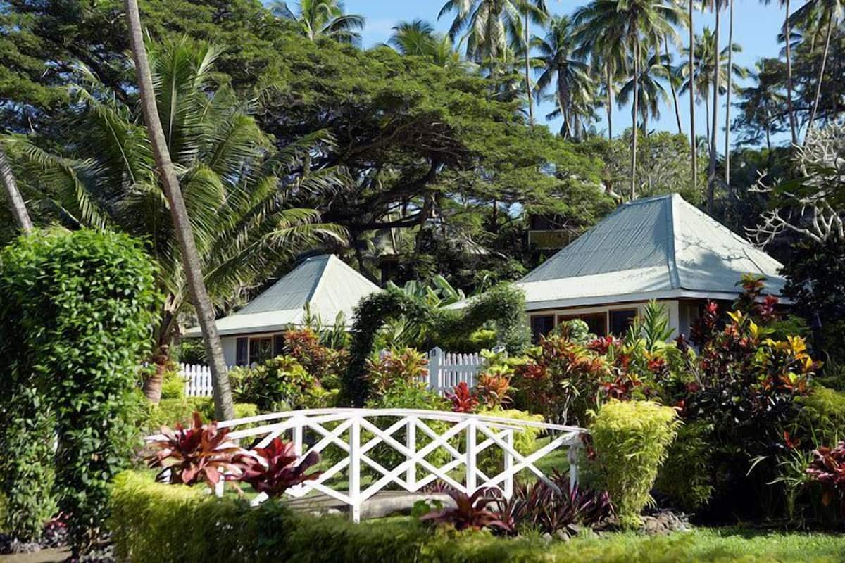 A two-story building with a white fence and lush tropical vegetation.