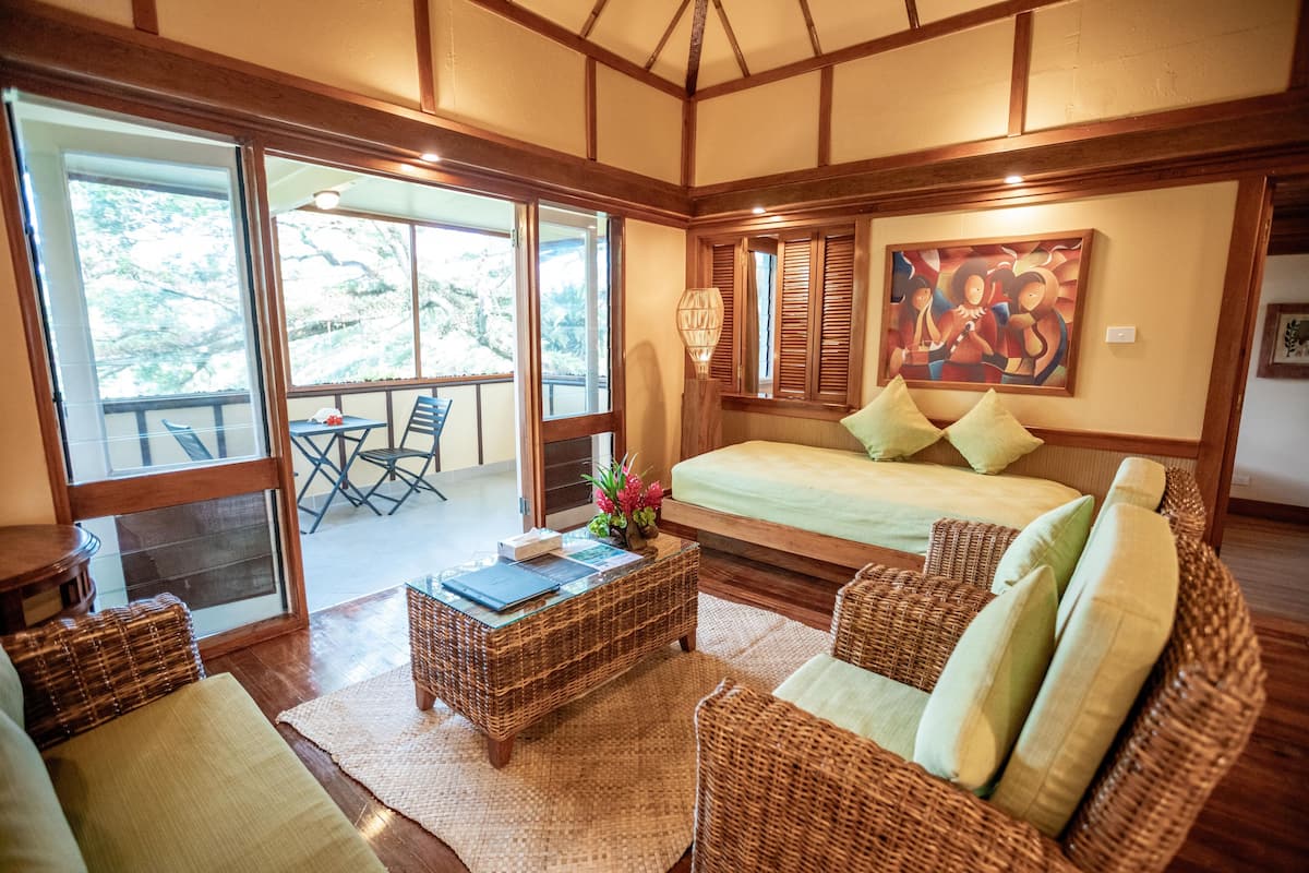 A spacious room with a large bed, wicker furniture, a dining table, and a painting on the wall.