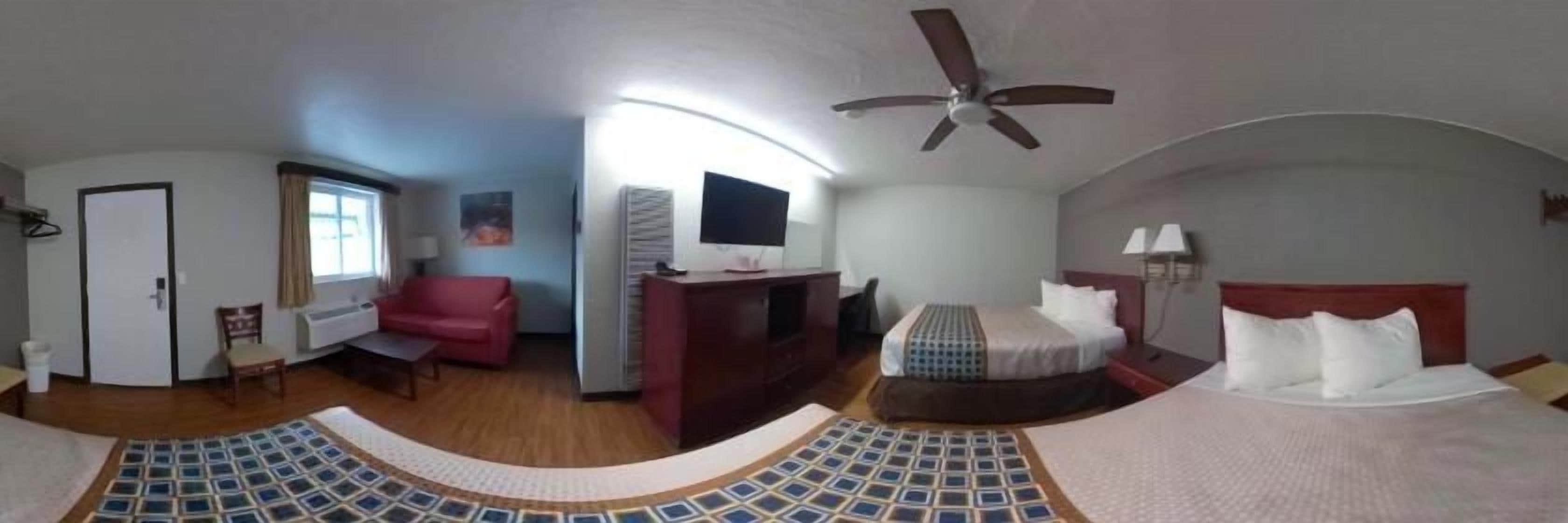 Una habitación con cama, escritorio, silla, televisor y ventilador de techo.