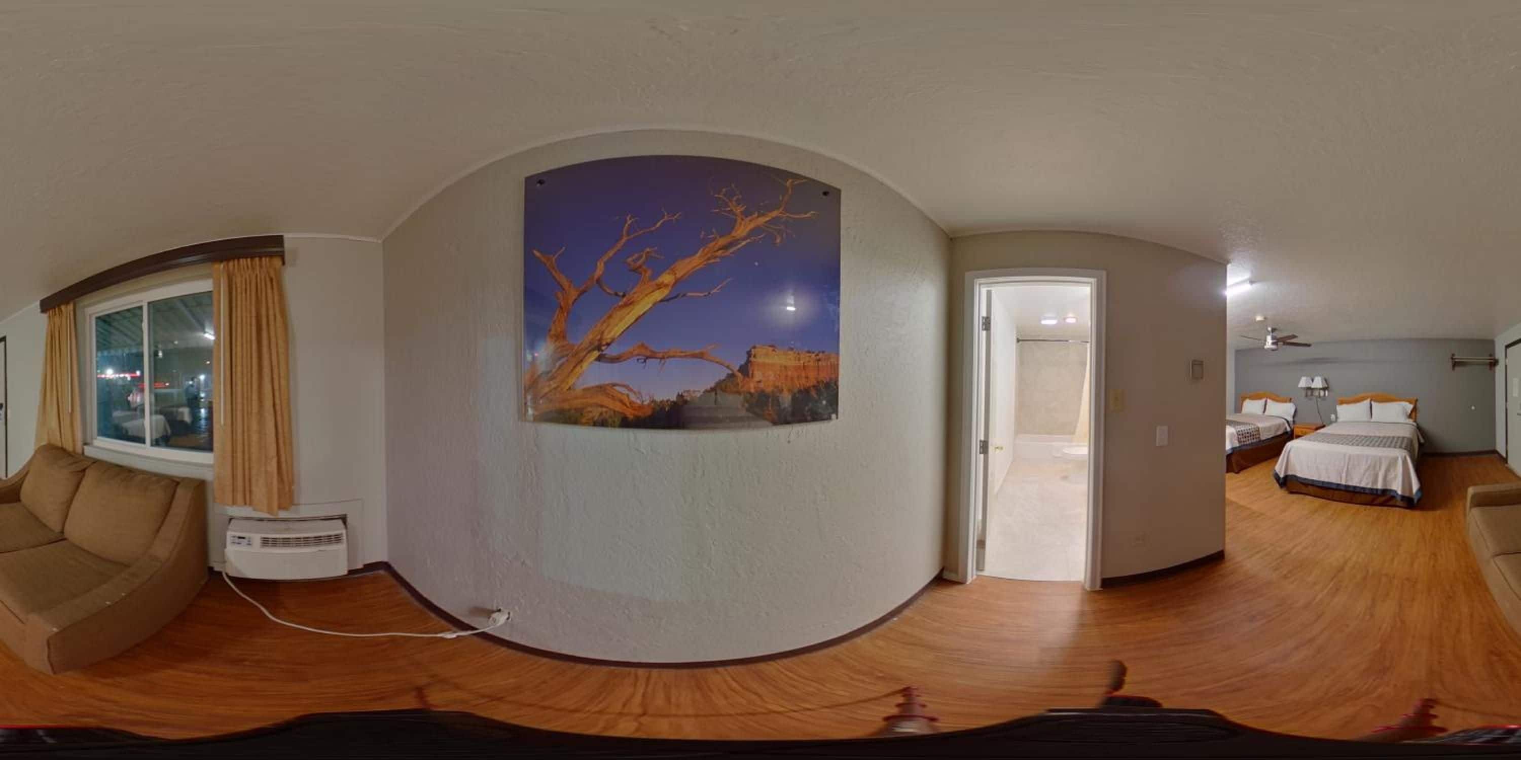 Une vue panoramique d’une chambre d’hôtel avec une grande fenêtre, un tableau représentant un arbre et un lit avec une table de chevet.